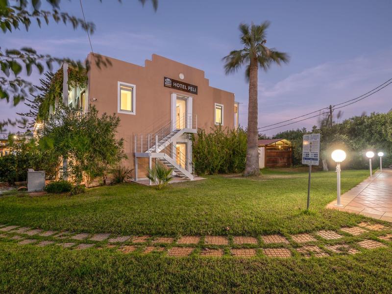 Bâtiment d'hôtel de deux étages avec palmier et pelouse au premier plan au crépuscule.