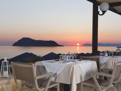 Terrasse mit gedeckten Tischen und Stühlen bei Sonnenuntergang mit Blick aufs Meer und eine Insel.