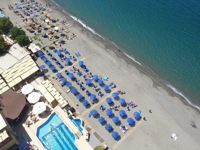 Vista aérea de una piscina de hotel y playa con sombrillas azules junto al mar.