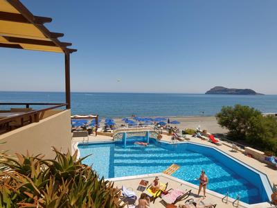 Hotelpool mit Blick auf das Meer, Liegestühle und Sonnenschirme am Strand unter blauem Himmel.