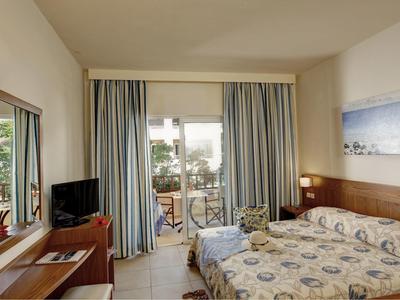 Habitación de hotel luminosa con dos camas individuales, escritorio, televisor y balcón con vista al mar.