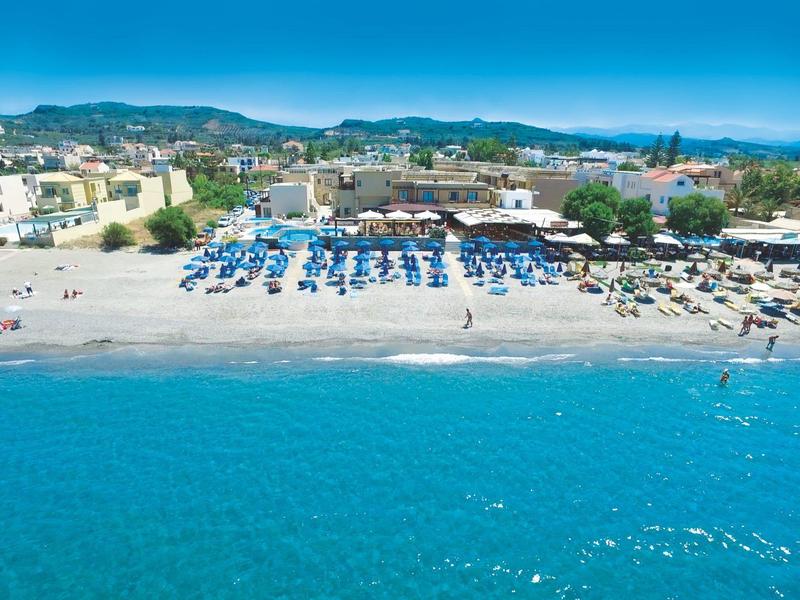 Playa con sombrillas y edificios junto al mar bajo un cielo azul en un destino turístico.