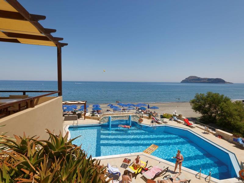 Piscina del hotel con huéspedes, sombrillas y vista al mar y una isla en el horizonte.