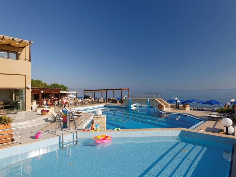 Piscina moderna de hotel con vista al mar, terraza soleada y cielo azul claro.