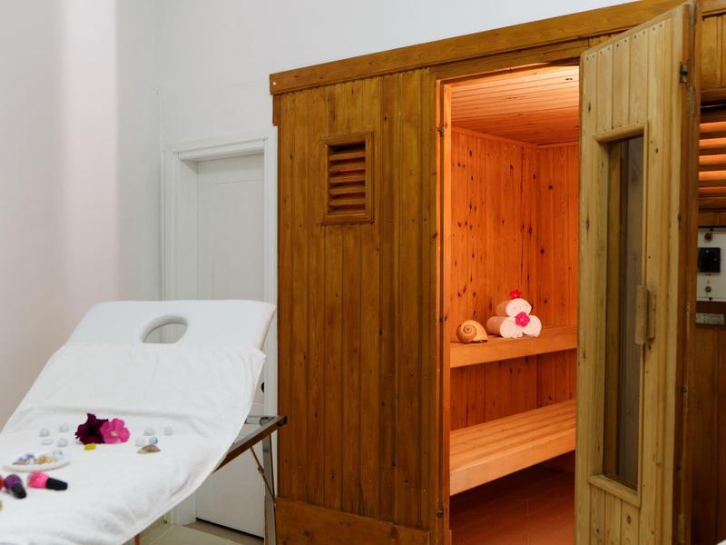 Sauna de madera con puerta abierta y camilla con flores en una zona de spa.