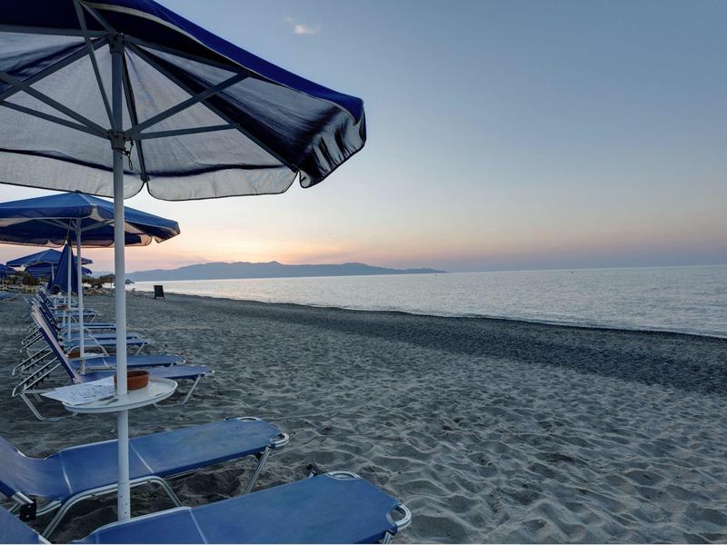 Playa vacía con tumbonas azules y sombrillas al atardecer junto al mar.