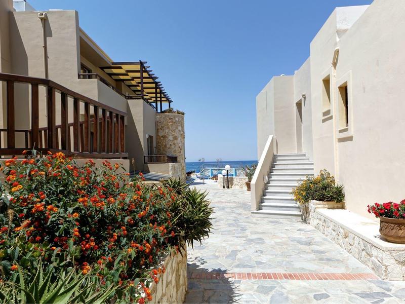 Camino iluminado del hotel con flores que conduce al mar bajo un cielo despejado.