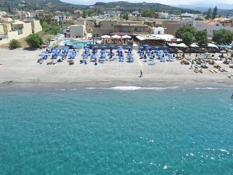 Playa con tumbonas azules y sombrillas frente a una localidad costera animada.