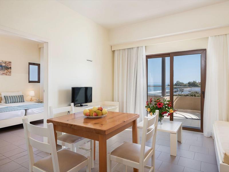 Sala luminosa con mesa, sillas, televisor y vista al balcón con vista al mar.