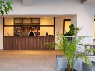 Moderner Hotelbarbereich mit Holztheke und Pflanzen in einem hellen Raum.