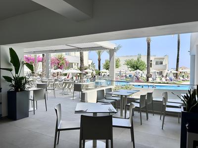 Blick von einer überdachten Terrasse auf einen Poolbereich mit Tischen und Stühlen unter Sonnenschirmen.