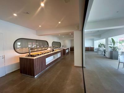 Modernes Hotelrestaurant mit Buffetstation und Sitzbereich mit großen Fenstern und Pflanzen.