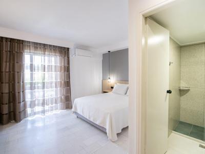 Simply furnished hotel room with double bed, curtains, and separate bathroom with shower.