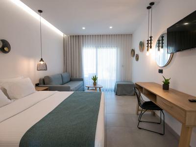 Modern hotel room with bed, desk, sofa, and TV in a neutral design.