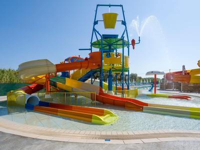 Colorful water slide park with large bucket and multiple slides outdoors under blue sky.