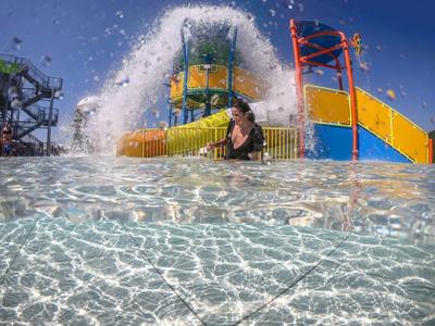 Person stands in clear water in front of colorful water slides at a water park.