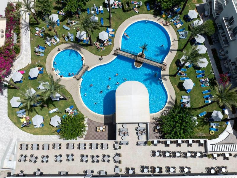 Aerial view of a large hotel swimming pool with lounge chairs and green palm trees.