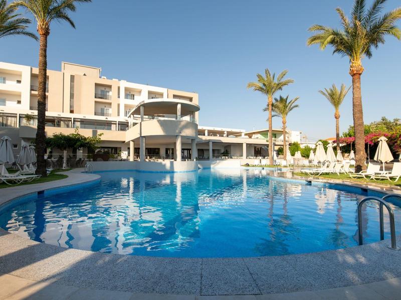 Round hotel pool with palm trees and lounge chairs under clear sky.
