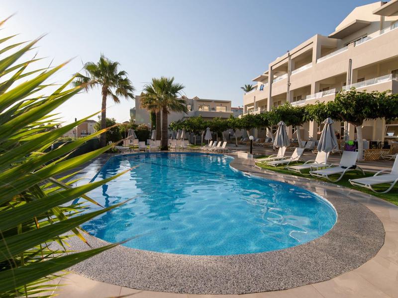 Modern hotel pool with sun loungers and umbrellas, surrounded by palm trees under a blue sky.