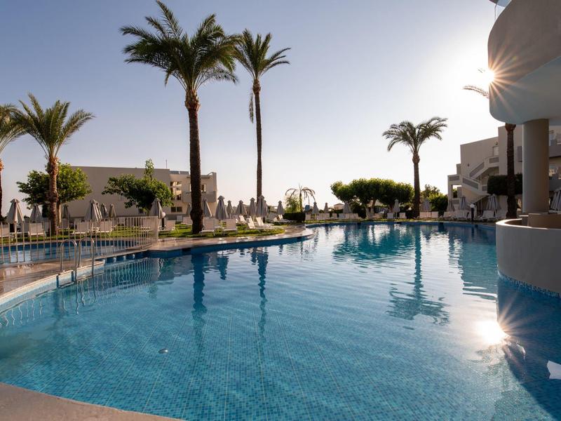 Swimming pool with palm trees and loungers at sunset in a holiday resort.