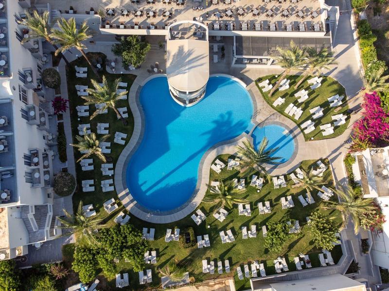 Aerial view of a hotel pool with sun loungers and green garden areas
