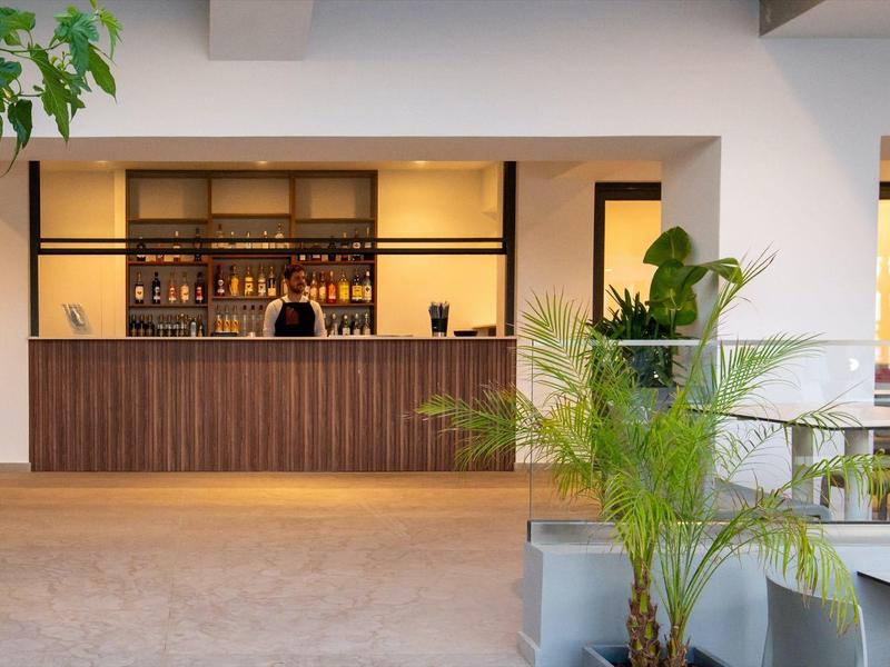 Modern hotel bar with wooden paneling and indoor plants.