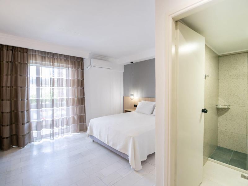 Simply furnished hotel room with double bed, curtains, and separate bathroom with shower.