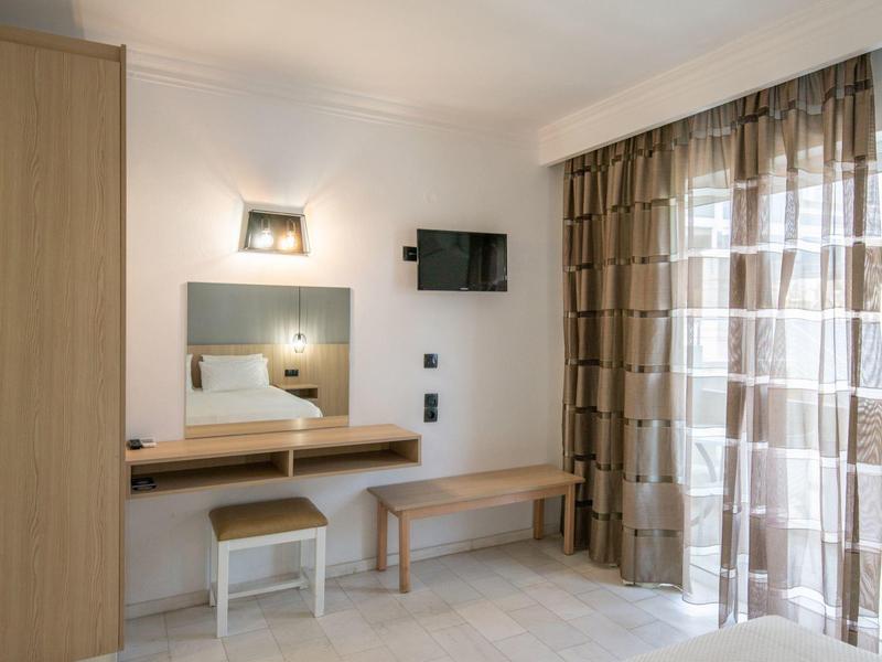 Bright hotel room with wooden furniture, mirror, TV, and window with brown curtains.