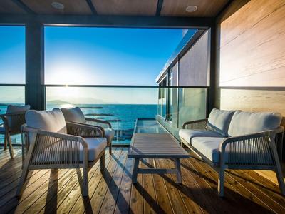 Balkon mit moderner Sitzgruppe aus Metall und Kissen, Blick auf Meer bei Sonnenuntergang.