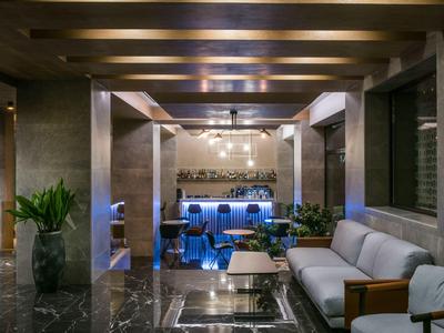 Modernes Hotel-Lounge mit Sitzbereich, Pflanzen und Bar im Hintergrund bei gedämpfter Beleuchtung.