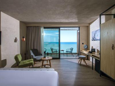 Modern hotel room with sea view, balcony, seating area, and wooden floor.
