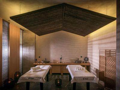 Calm spa room with two massage tables, soft lighting, and wooden accents.