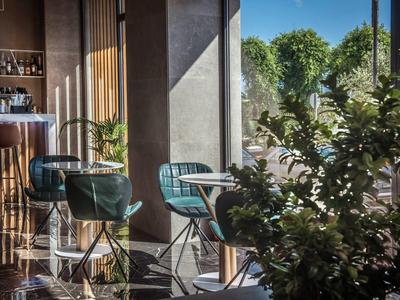 Espace bar d'hôtel moderne avec chaises et tables, éclairé par la lumière naturelle du soleil.