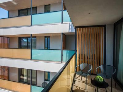 Balcon d'hôtel moderne avec balustrade en verre, deux chaises et une petite table avec plante.
