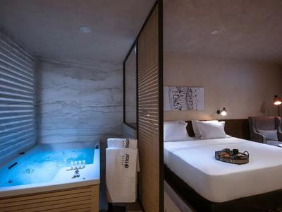 Chambre d'hôtel moderne avec grand lit et jacuzzi dans une zone séparée.