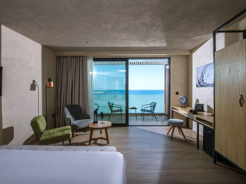 Modern hotel room with sea view, balcony, seating area, and wooden floor.