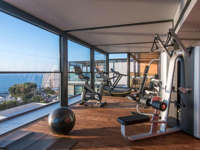 Modern gym with sea view and wooden floor in a hotel.
