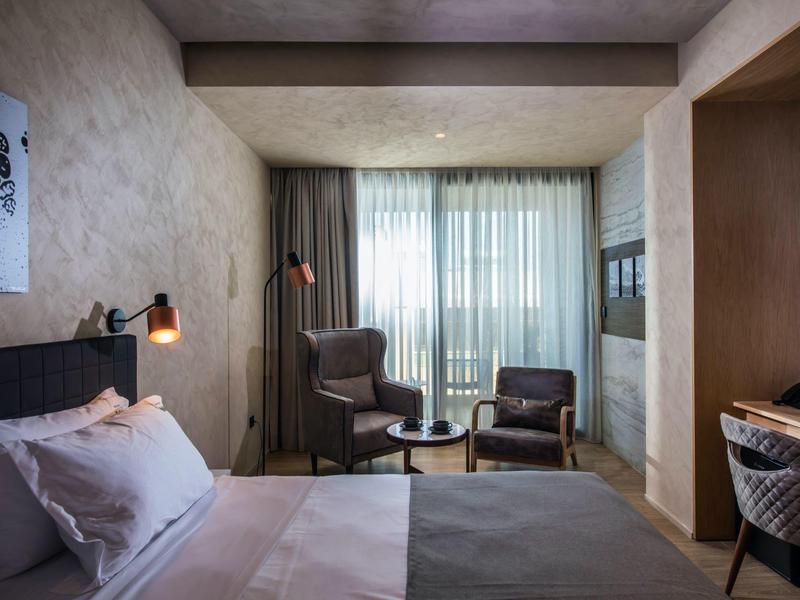 Cozy hotel room with double bed, armchairs, and large window with curtains.