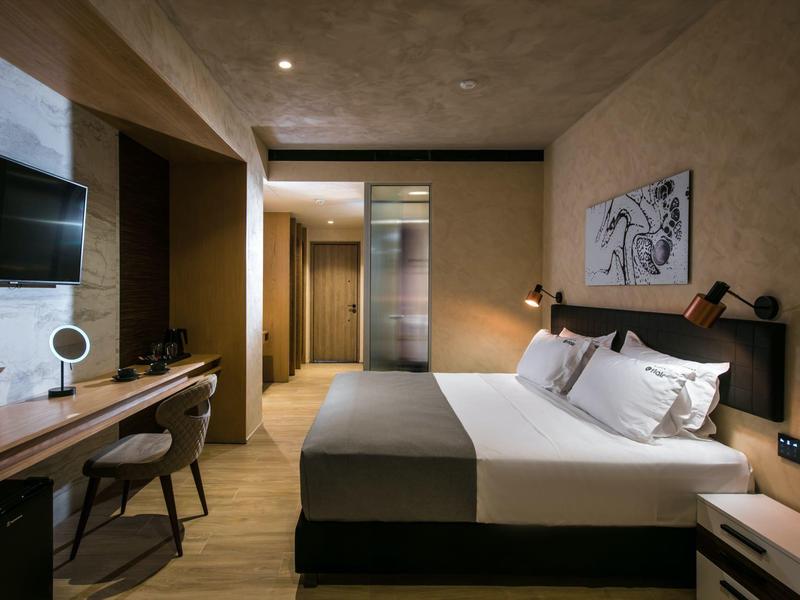 Modern hotel room with double bed, desk, chair, and minimalist decor.