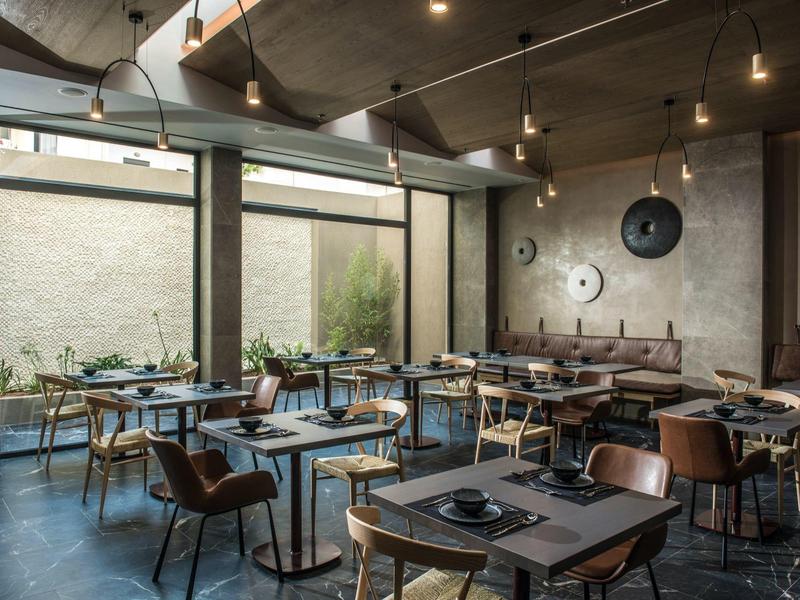 Modern restaurant with dark tables, comfortable chairs, and large windows overlooking outside.