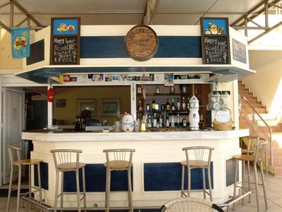 Kleine Bar mit weißen Stühlen und einem hölzernen Tresen unter einem überdachten Bereich.