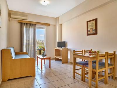 Světý obývací pokoj s pohovkou, jídelním stolem, televizí a balkonem s výhledem na město a hory.