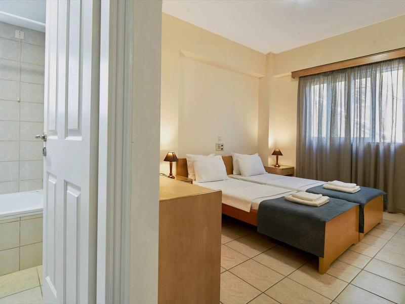 Světý hotelový pokoj se dvěma jednolůžky, nočními stolky, taburety a přilehlou koupelnou