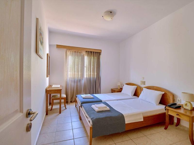 Jasná ložnice se dvěma lůžky, nočními stolky a oknem se závěsy.