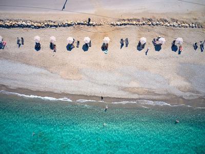 Vogelperspektive eines Strandes mit klartem Wasser und in Reihen stehenden Sonnenschirmen.