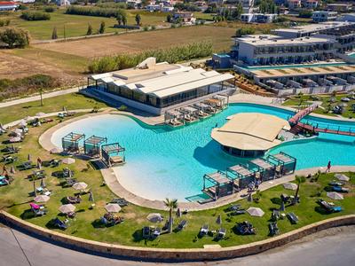 Großer Hotelpool mit Liegestühlen und Rasenflächen, umgeben von Gebäuden und Straße.