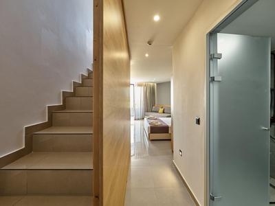 Moderner Hotelflur mit Treppe links, Glastür rechts und Blick ins helle Schlafzimmer.