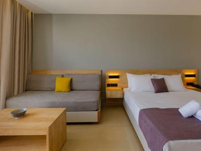 Modern eingerichtetes Hotelzimmer mit Doppelbett, Couch und Holzmöbeln in neutralen Farben.