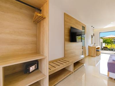 Modern eingerichtetes Hotelzimmer mit Fernseher, Safe und Balkon mit Aussicht auf grüne Landschaft.