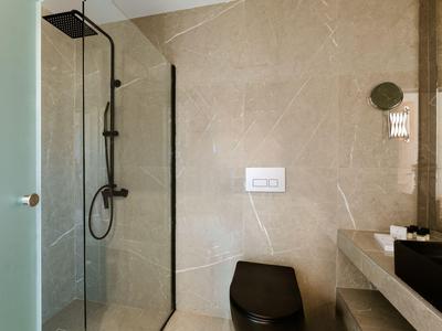 Modernes Badezimmer mit beiger Marmorwand, schwarzer Toilette und Glasdusche.